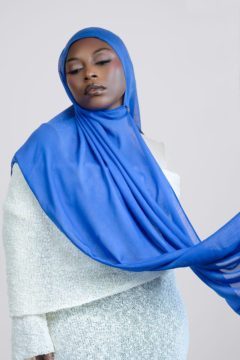 Woman wearing a blue hijab against a white background